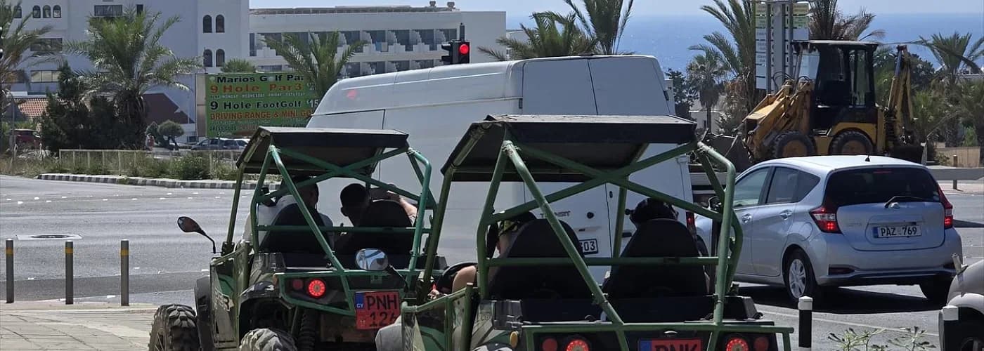 Two green off-road buggies seen from behind, beside a road in a coastal town